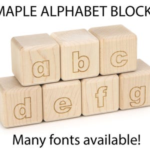 May include: Seven light-colored maple wood alphabet blocks arranged in two rows, featuring the engraved lowercase letters a, b, c, d, e, f, and g. The text MAPLE ALPHABET BLOCKS appears at the top and Many fonts available! at the bottom.