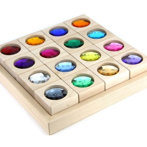 May include: A wooden tray with 16 individual compartments, each containing a colorful, faceted gem. The gems are arranged in a rainbow pattern.