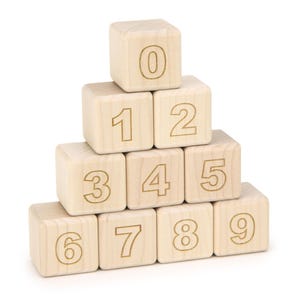 May include: A pyramid stack of ten light-colored wooden cubes, each featuring a single engraved numeral from zero to nine. The blocks are arranged in four rows, with the zero block at the top and the six through nine blocks forming the base.