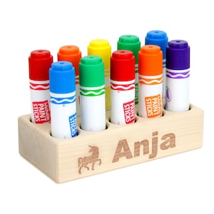 May include: A wooden paint stick holder with a unicorn design and the name "Anja" engraved on the front. The holder has eight slots and is filled with colorful washable paint sticks.
