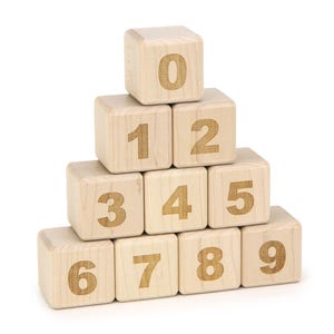 May include: A pyramid stack of ten light-colored wooden blocks, each featuring a single dark brown digit from zero to nine printed on the front face. The blocks are arranged in four rows, with the zero at the top and the nine at the bottom right.