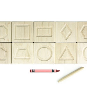 May include: A set of ten wooden blocks, each with a different shape carved into the top surface. The shapes include a circle, square, rectangle, diamond, pentagon, hexagon, oval, triangle, and two different types of trapeziums. A pink crayon and a wooden stylus are also included.