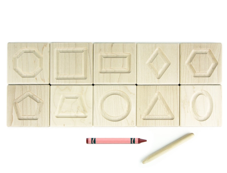 May include: A set of ten wooden blocks, each with a different shape carved into the top surface. The shapes include a circle, square, rectangle, diamond, pentagon, hexagon, oval, triangle, and two different types of trapeziums. A pink crayon and a wooden stylus are also included.