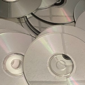May include: A stack of silver-colored compact discs, some with a rainbow iridescent sheen.