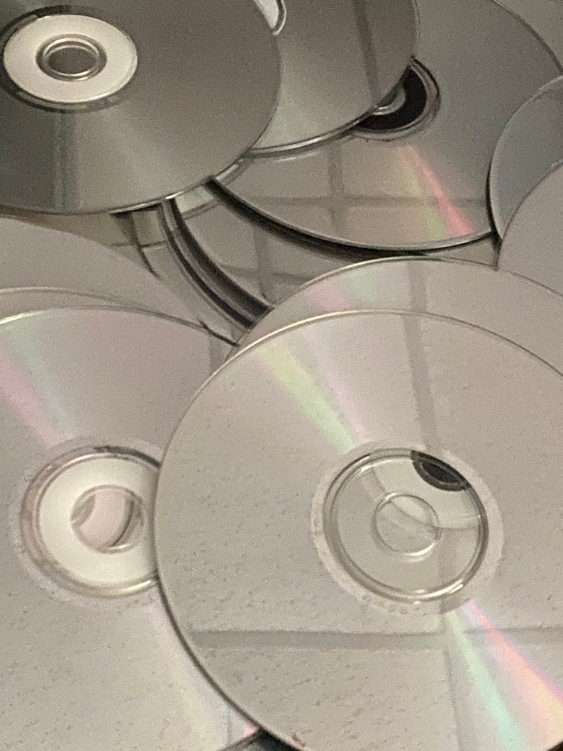 May include: A stack of silver-colored compact discs, some with a rainbow iridescent sheen.