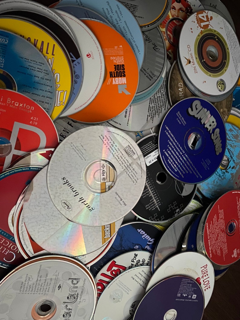 May include: A pile of various CDs, some with colorful labels and others with black and white labels. The CDs are stacked on top of each other, creating a chaotic and colorful scene.