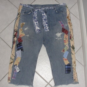 May include: Blue denim jeans with a patchwork design on the sides. The patchwork includes floral, plaid, and geometric patterns in various colors.