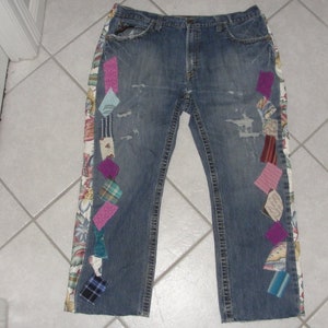 May include: Blue denim jeans with a patchwork design on the sides. The patches are made of various fabrics in pink, purple, green, and white.