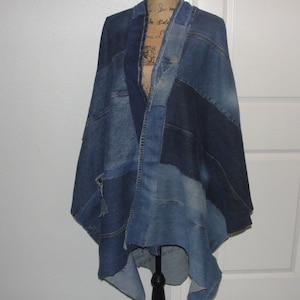 May include: A denim poncho made from repurposed denim fabric. The poncho is blue and has a patchwork design. It is asymmetrical and has a long, flowing hem.