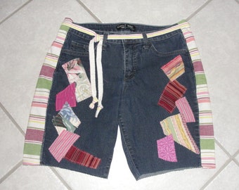 Puede incluir: Pantalones cortos de mezclilla azul con un cordón blanco y parches de tela coloridos cosidos en la parte delantera y los lados. Los lados de los pantalones cortos tienen rayas blancas, rosadas y verdes.