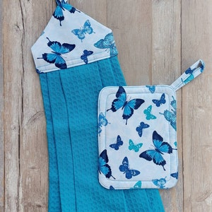 May include: A set of two kitchen towels with a blue and white butterfly print. The hand towel has a loop for hanging and the pot holder has a loop for hanging.