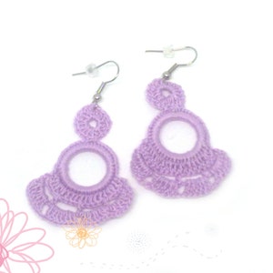 May include: A pair of lavender crocheted earrings with a large circle design and a smaller circle at the top. The earrings are attached to silver hooks.