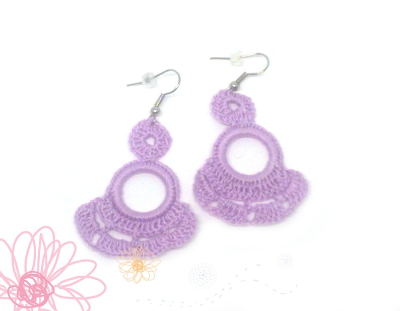 May include: A pair of lavender crocheted earrings with a large circle design and a smaller circle at the top. The earrings are attached to silver hooks.