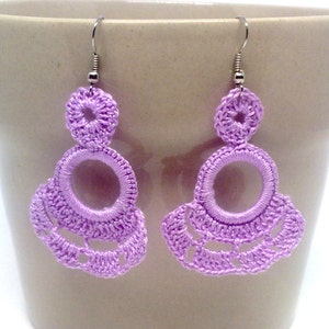 May include: A pair of lavender crocheted earrings with a circle design. The earrings are hanging from silver hooks.
