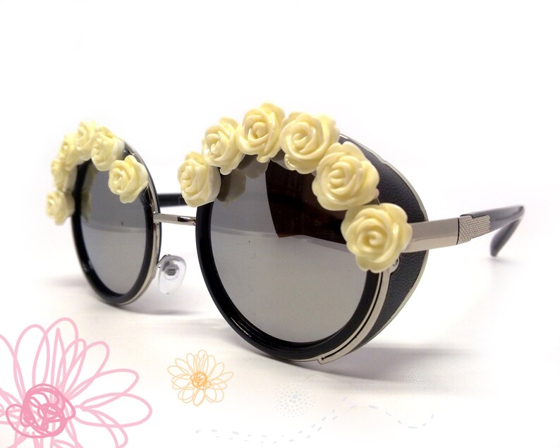 May include: Round black sunglasses with a silver metal frame and a row of white plastic flowers across the top.