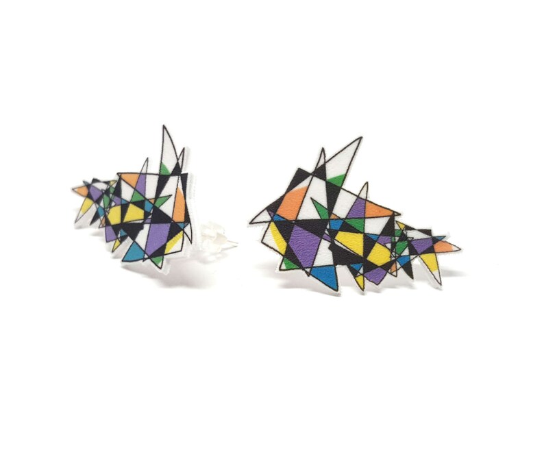 May include: A pair of colorful geometric earrings with a black outline. The earrings are made of acrylic and have a modern, abstract design.