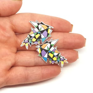 May include: A pair of colorful geometric earrings with a white background. The earrings are made of a variety of shapes and sizes, including triangles, squares, and circles. The colors are bright and vibrant, including yellow, blue, green, purple, and orange.