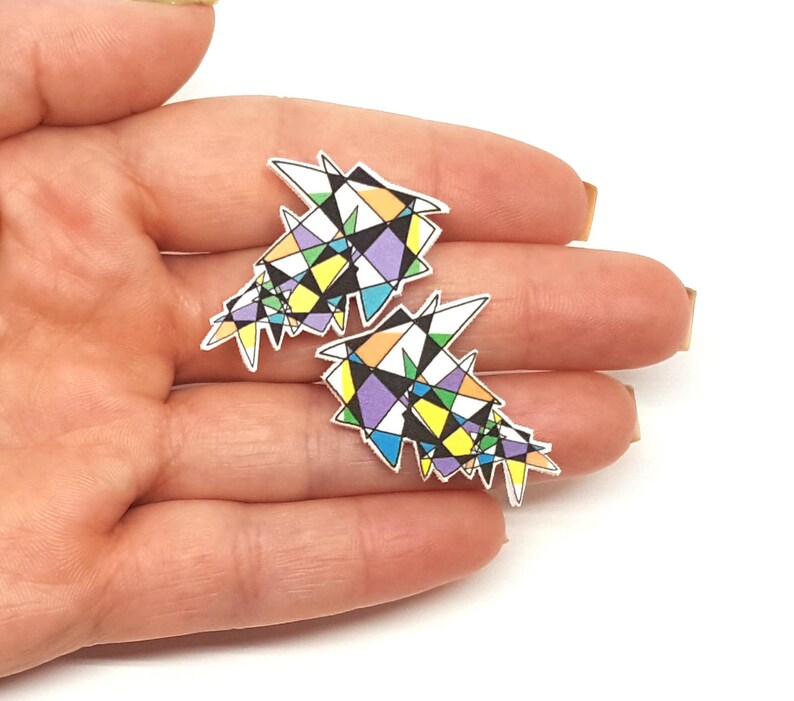 May include: A pair of colorful geometric earrings with a white background. The earrings are made of a variety of shapes and sizes, including triangles, squares, and circles. The colors are bright and vibrant, including yellow, blue, green, purple, and orange.
