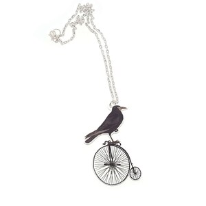 May include: A silver necklace with a black crow riding a unicycle pendant.