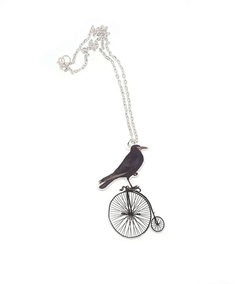 May include: A silver necklace with a black crow riding a unicycle pendant.