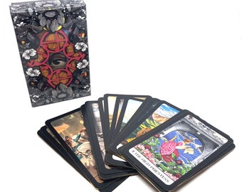 May include: A deck of tarot cards with black borders and colorful illustrations. The cards are fanned out to show the images. The top card shows a woman in a pink dress standing in a doorway with a blue sky and clouds behind her. The text on the card reads "II The High Priestess".