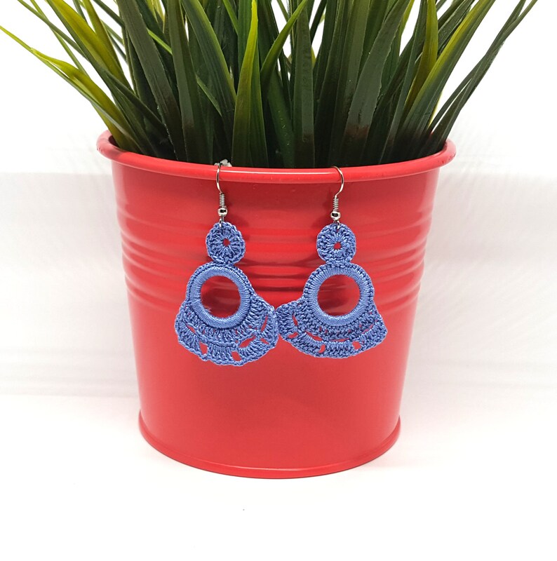 May include: A pair of crocheted earrings in a light blue color. The earrings have a circular design with a smaller circle in the center. The earrings are hanging from silver hooks.