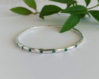 May include: A silver bangle bracelet with a hammered finish and small green gemstones set around the band.