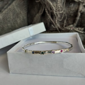May include: A silver bangle bracelet with a hammered texture and five colourful gemstones set into the metal.