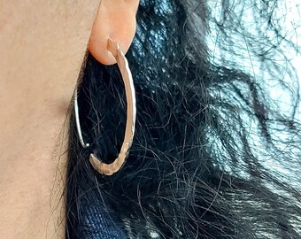 Puede incluir: Pendientes de aro de plata con textura martillada. Los pendientes se llevan en la oreja de una persona.