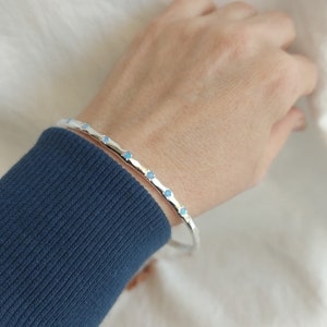May include: A silver bangle bracelet with small blue gemstones set around the edge.