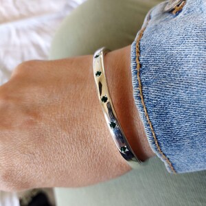 May include: A silver bangle bracelet with a row of small, dark green gemstones.