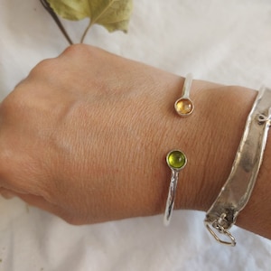 May include: A silver bangle bracelet with two round glass stones, one green and one amber, set into the metal.