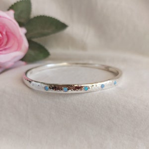 May include: A silver bangle bracelet with a hammered finish and five small blue opal stones set in the band.