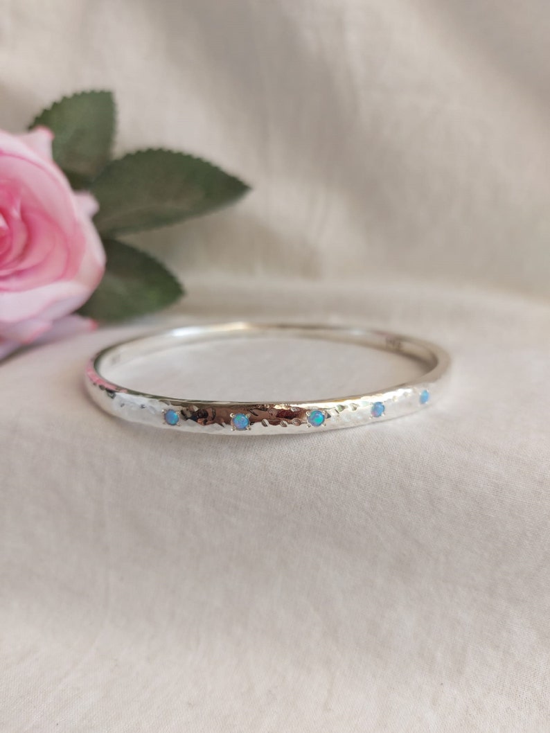 May include: A silver bangle bracelet with a hammered finish and five small blue opal stones set in the band.