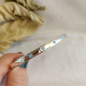 May include: A silver hammered bangle bracelet with a row of small opal gemstones.