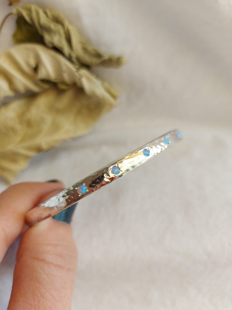 May include: A silver hammered bangle bracelet with a row of small opal gemstones.