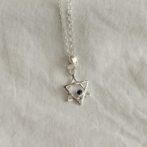 May include: A silver chain necklace with a silver Star of David pendant featuring a small blue gemstone in the centre.