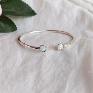 Puede incluir: Un brazalete de plata con dos piedras de ópalo blancas. El brazalete tiene una textura martillada.