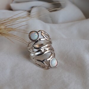 May include: A silver ring with a unique, branch-like design. The ring features two white opal stones.