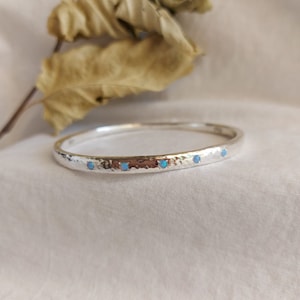 May include: A silver bangle bracelet with a hammered texture and four small blue opal stones set in a row.
