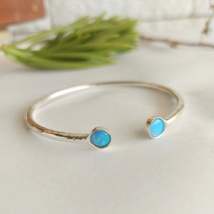 May include: A silver hammered bangle bracelet with two blue opal stones.