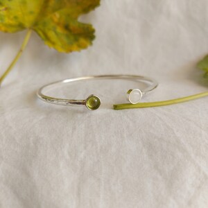 Può includere: Un braccialetto rigido in argento con finitura martellata e due pietre rotonde, una verde e una bianca.