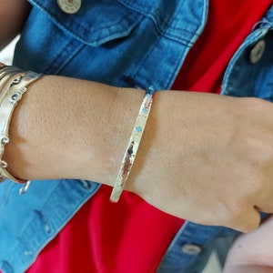 May include: A silver hammered bangle bracelet with small turquoise stones set into the metal. The bracelet is worn on a person's wrist.