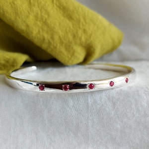 May include: A silver bangle bracelet with four small red gemstones set into the metal.