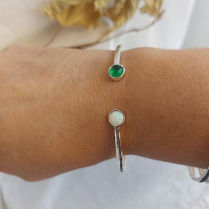 May include: A silver bangle bracelet with a green and white gemstone accent. The bracelet is open and has a hammered texture.