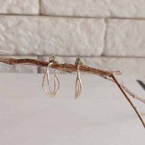 K&ouml;nnte beinhalten: Ein Paar silberfarbene Ohrringe mit filigranem Design. Jeder Ohrring hat eine l&auml;ngliche Tropfenform, wobei drei gebogene Linien die Hauptstruktur bilden. Die Ohrringe werden auf einem d&uuml;nnen, braunen Ast vor wei&szlig;em Hintergrund pr&auml;sentiert.