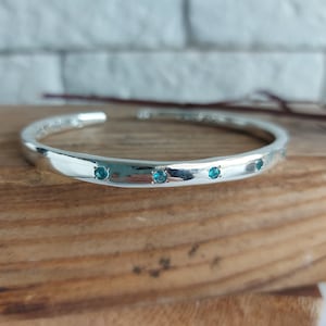 Puede incluir: Un brazalete de plata con acabado martillado y cinco pequeñas piedras turquesa.