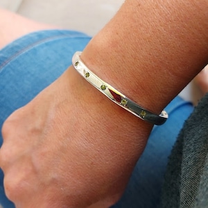 May include: A silver bangle bracelet with small green gemstones set into the band.