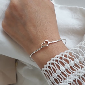 Pode incluir: Um bracelete de prata com acabamento martelado e um recorte em forma de coração. O bracelete é aberto e ajustável.
