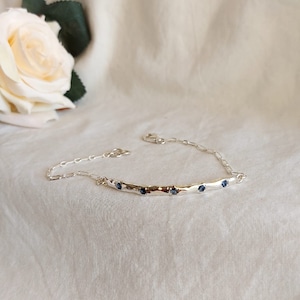 Może przedstawiać: Srebrna bransoletka z młotkowanym, zakrzywionym wzorem i pięcioma niebieskimi kamieniami szlachetnymi.